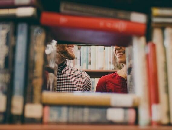Man and woman standing behind a bookshelf and smiling at each other | Host Family Stay